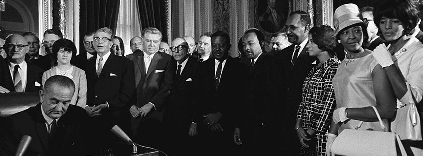 President Lyndon B. Johnson signs the Voting Rights Act of 1965 while Sen. Everett Dirksen, Dr. Martin Luther King, Jr. and others look on.