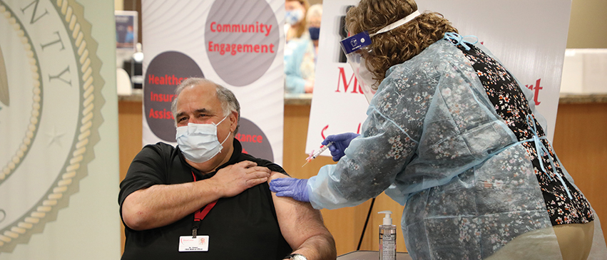 Dr. Gregg Stoner, medical director at Heartland Health Services, rolls up his sleeve for the COVID-19 vaccine at Heddington Oaks in West Peoria.