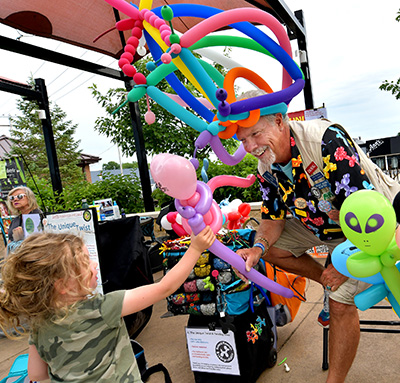 Man handing a balloon creation to a young girl.