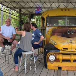 Photo of customers enjoying drink on a deck next to an old school bus