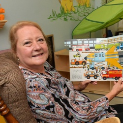 Woman sitting in a recliner holding up a picture book