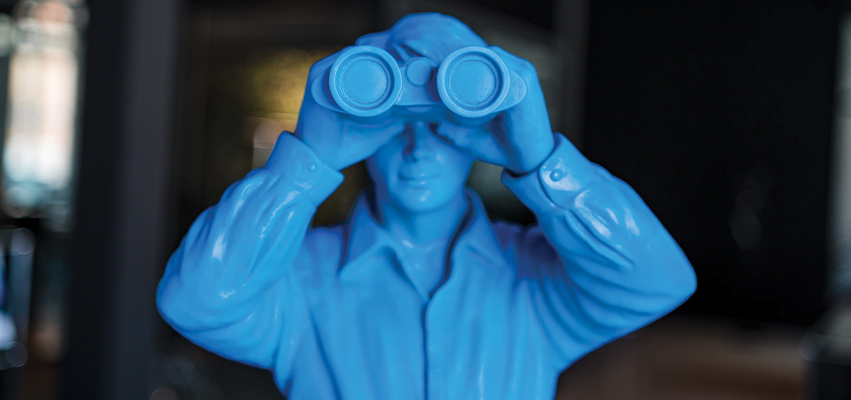 Photo of a blue plastic toy man looking thru binoculars