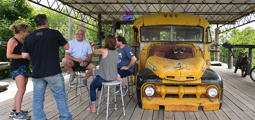 Photo of customers enjoying drink on a deck next to an old school bus