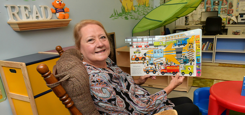 Woman sitting in a recliner holding up a picture book