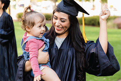 Woman in a graduation cap and gown, holding a child