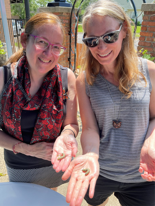 Celeste Restrepo and artist Linda Webb holding caterpillars, part of a hands-on event featuring butterfly art projects.