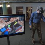 Using the HTC VIVE headset and handheld controllers, Wright attempts to pick up a “rock” in a 3D simulated Martian environment, as displayed on the screen.