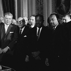 President Lyndon B. Johnson signs the Voting Rights Act of 1965 while Sen. Everett Dirksen, Dr. Martin Luther King, Jr. and others look on.